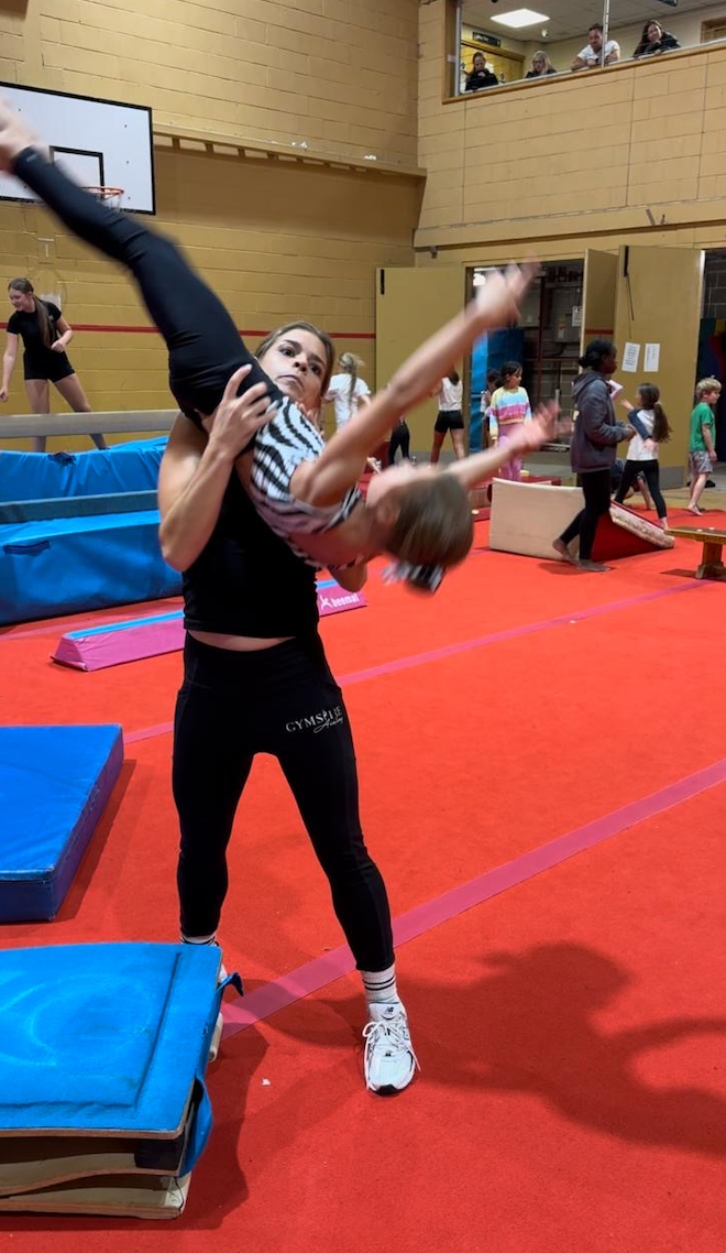 A woman is carrying a child on her shoulders in a gym.