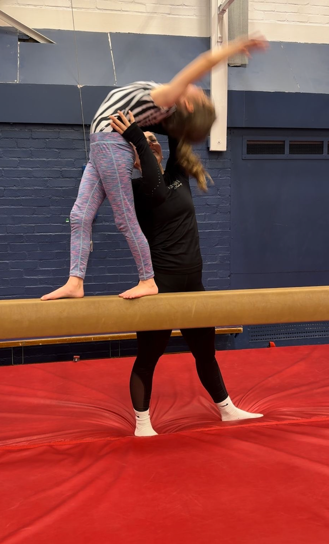 Two girls are standing on a balance beam in a gym.