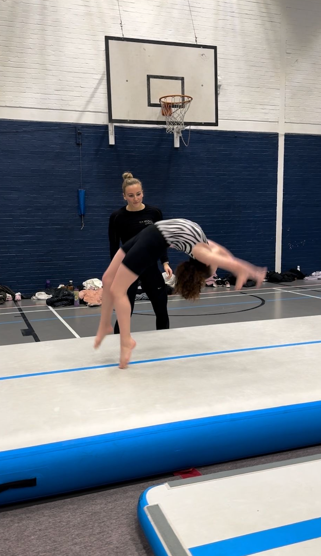 A girl is doing a handstand on a mat in a gym.