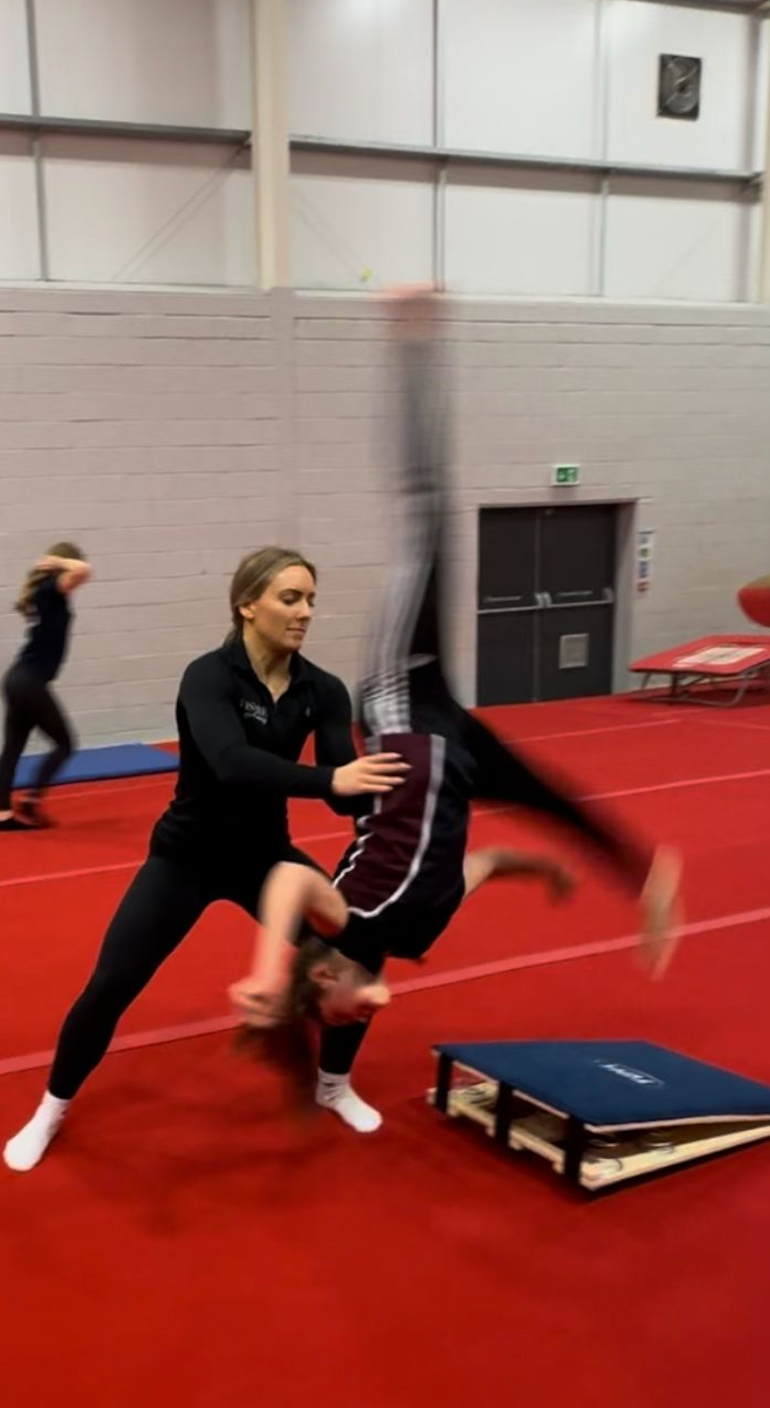 A woman is helping a young girl do a handstand on a trampoline.