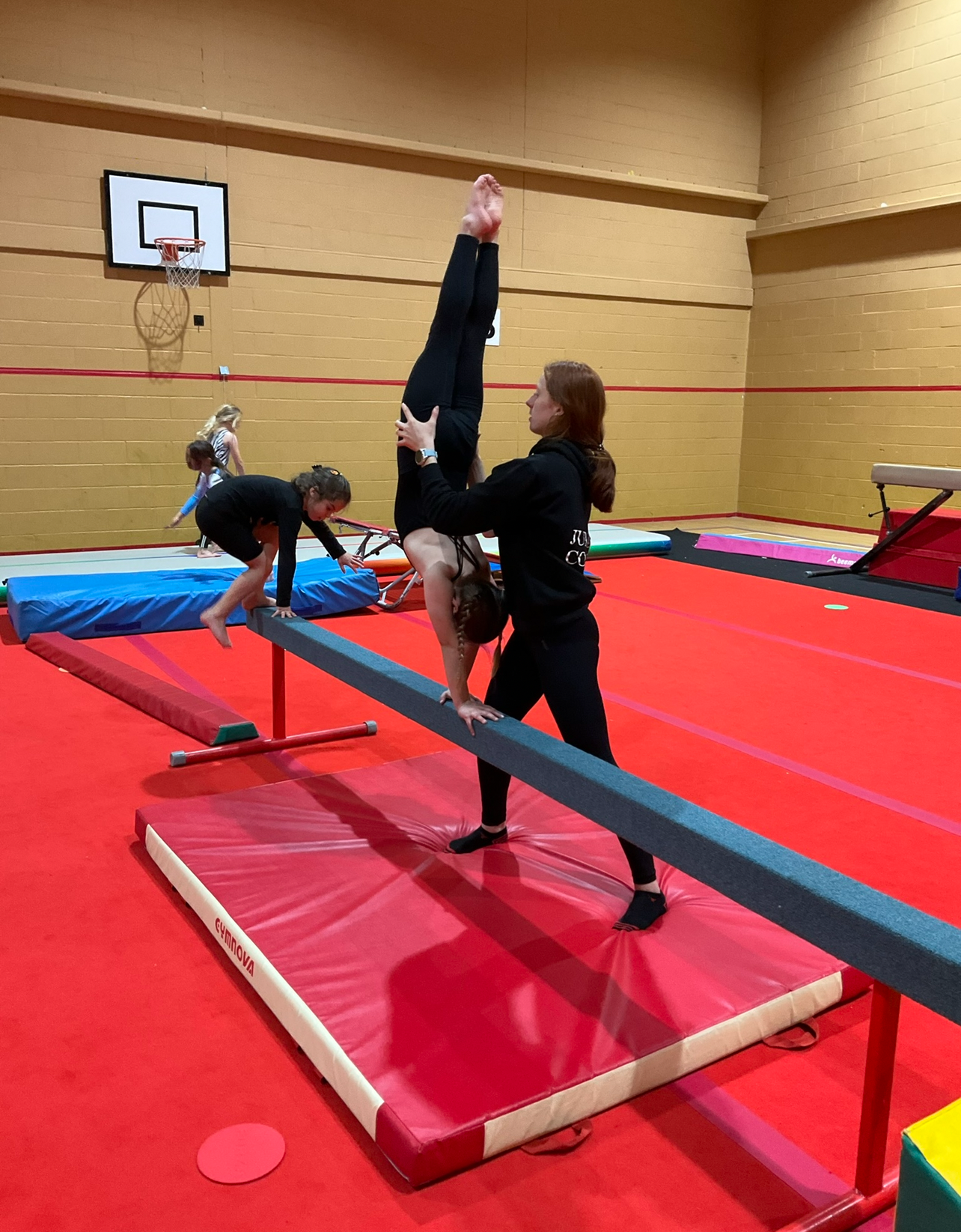 A woman is helping a young girl do a handstand on a balance beam.