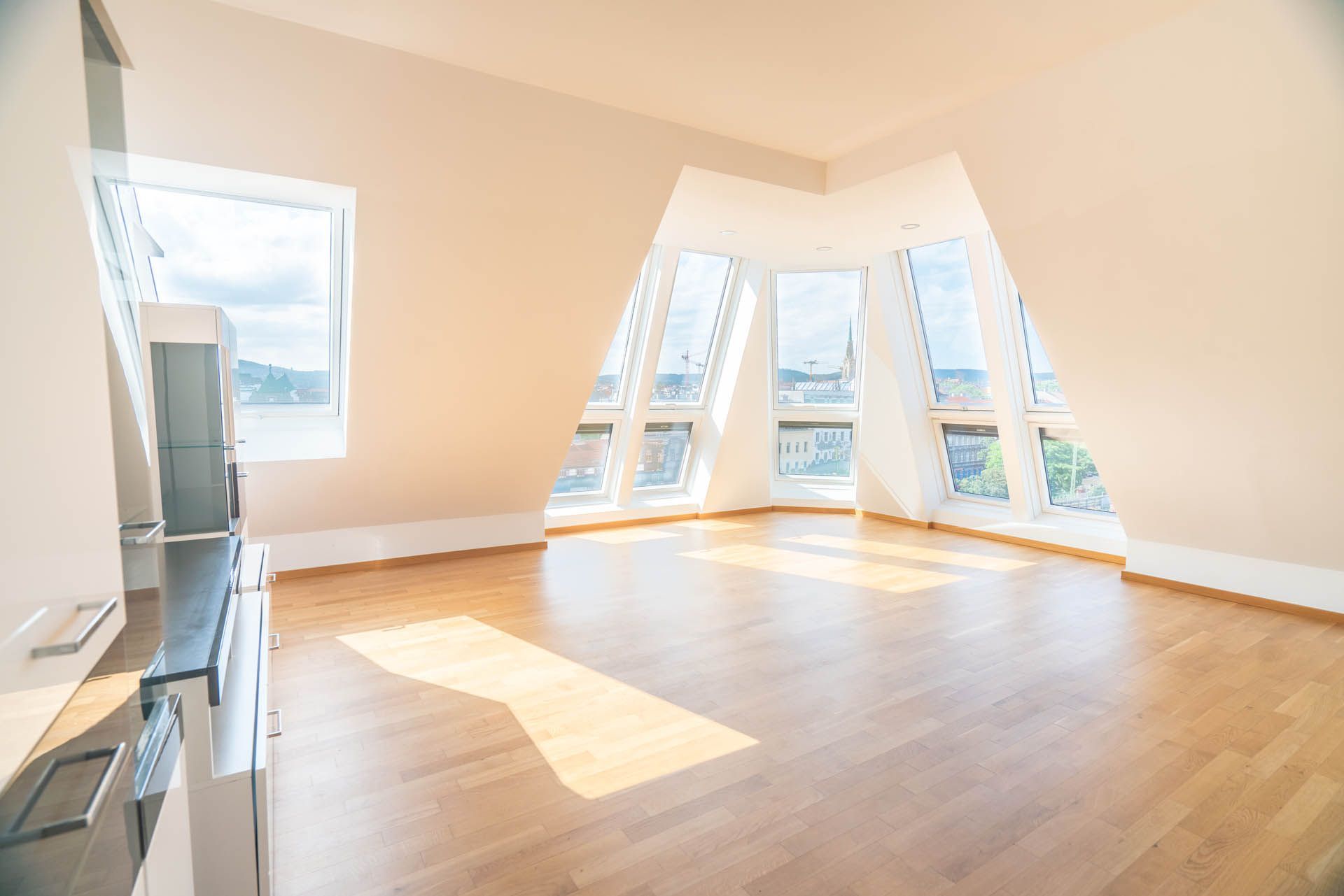 Leerer, sonnendurchfluteter Dachbodenraum mit hellen Holzböden und dreieckigen Fenstern.