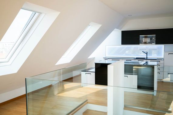 Helle, moderne Küche im Dachgeschoss mit Oberlichtern und Glasgeländer. Weiße und schwarze Schränke. Holzboden.