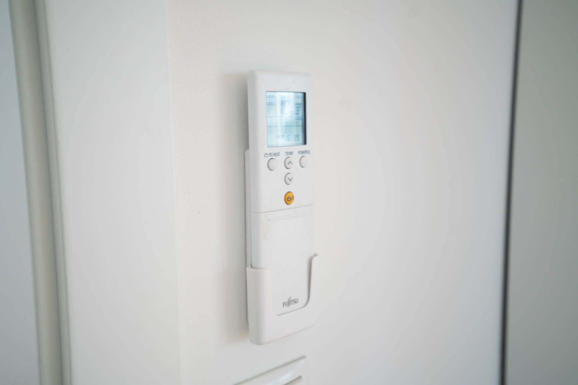 Weiße, wandmontierte Fernbedienung für die Klimaanlage mit Tasten und Display.