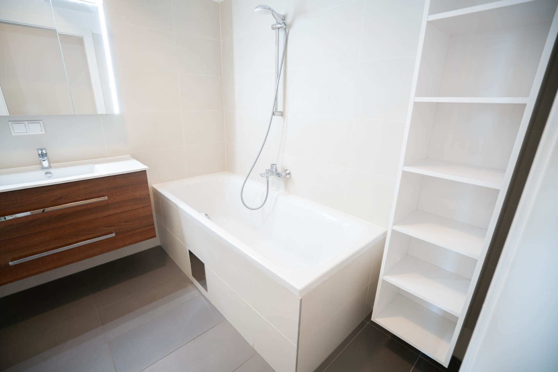 Badezimmer mit weißer Badewanne, Regalen und Holzwaschtisch.