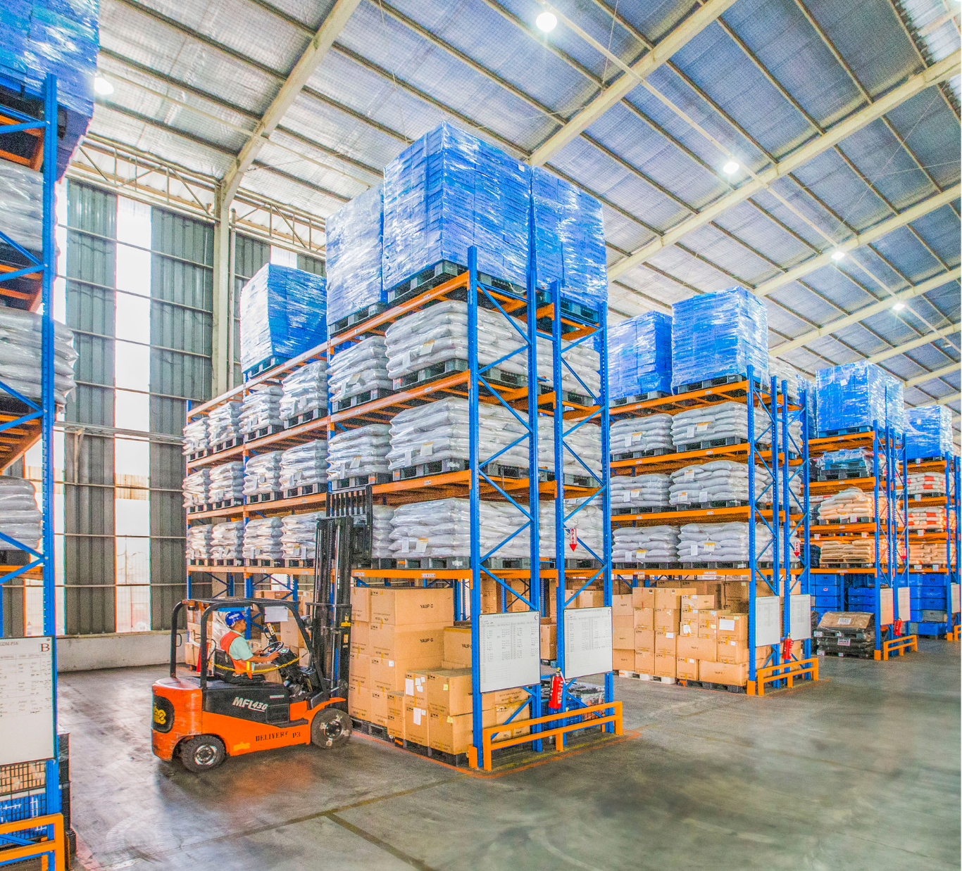 Forklift loading pallets stacked with boxes and blue-wrapped goods in a warehouse.