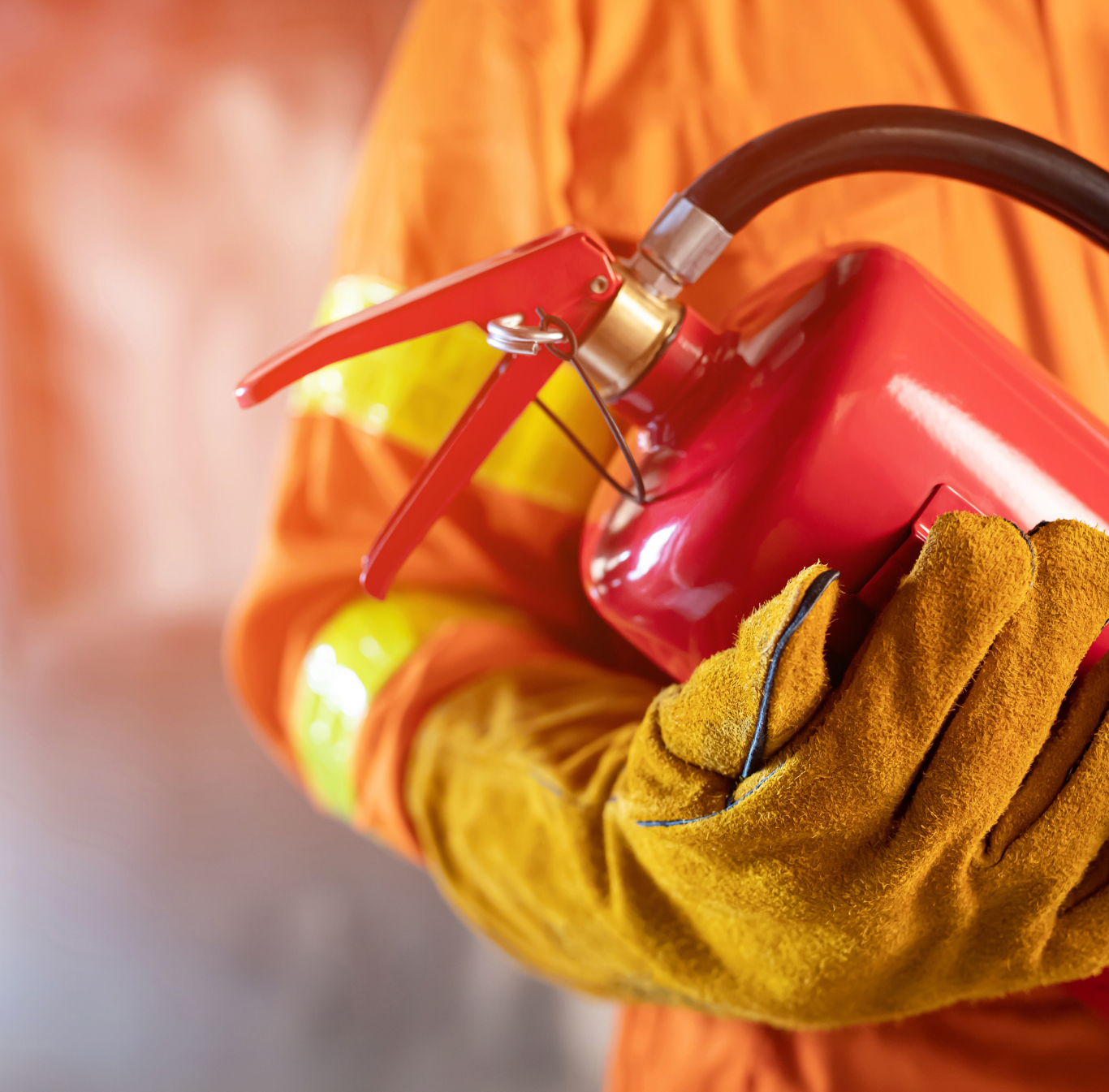 Firefighter in orange gear and yellow gloves holding a red fire extinguisher.