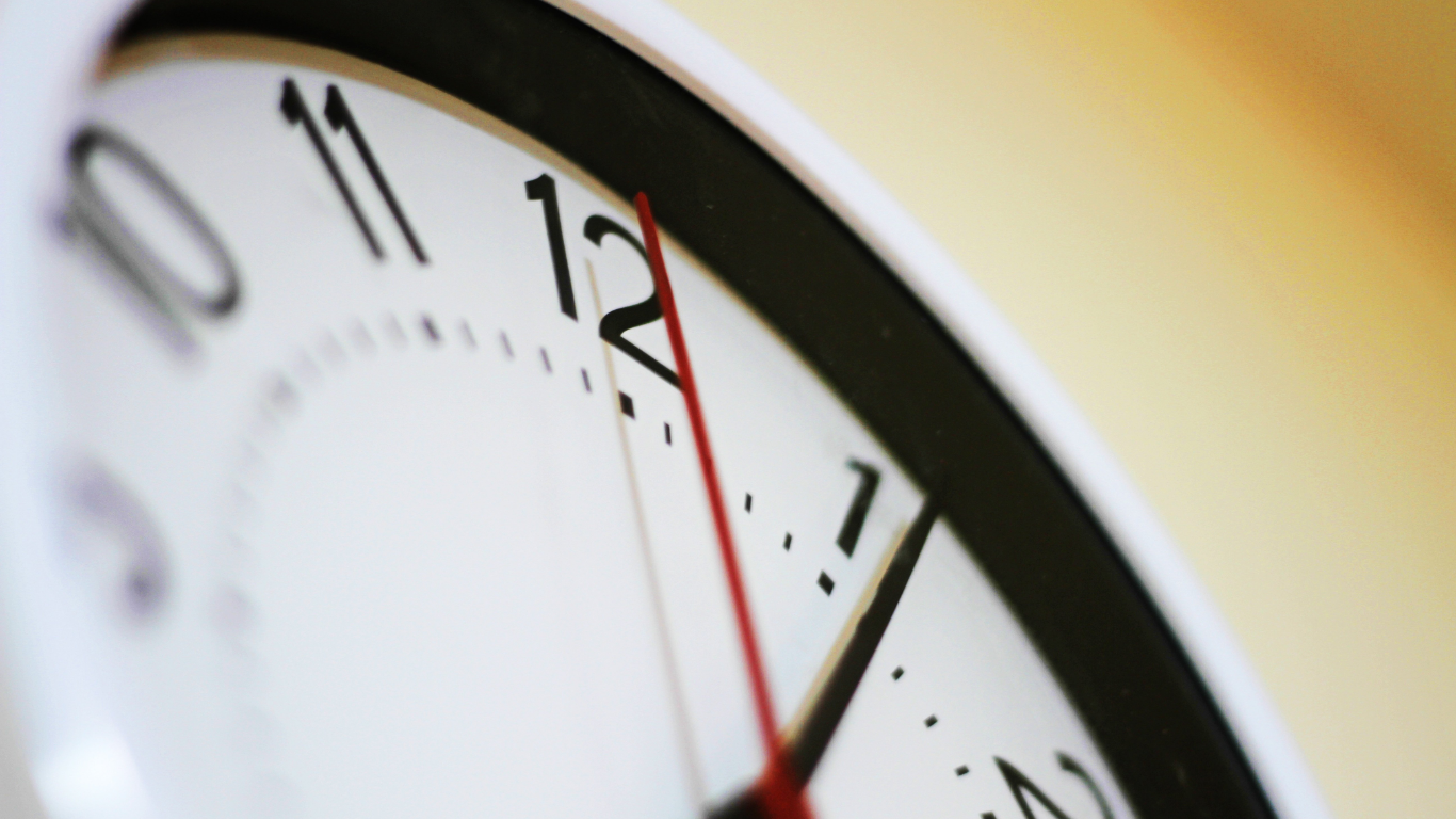Clock face with red second hand near 12, black hands near 12:01, white background.