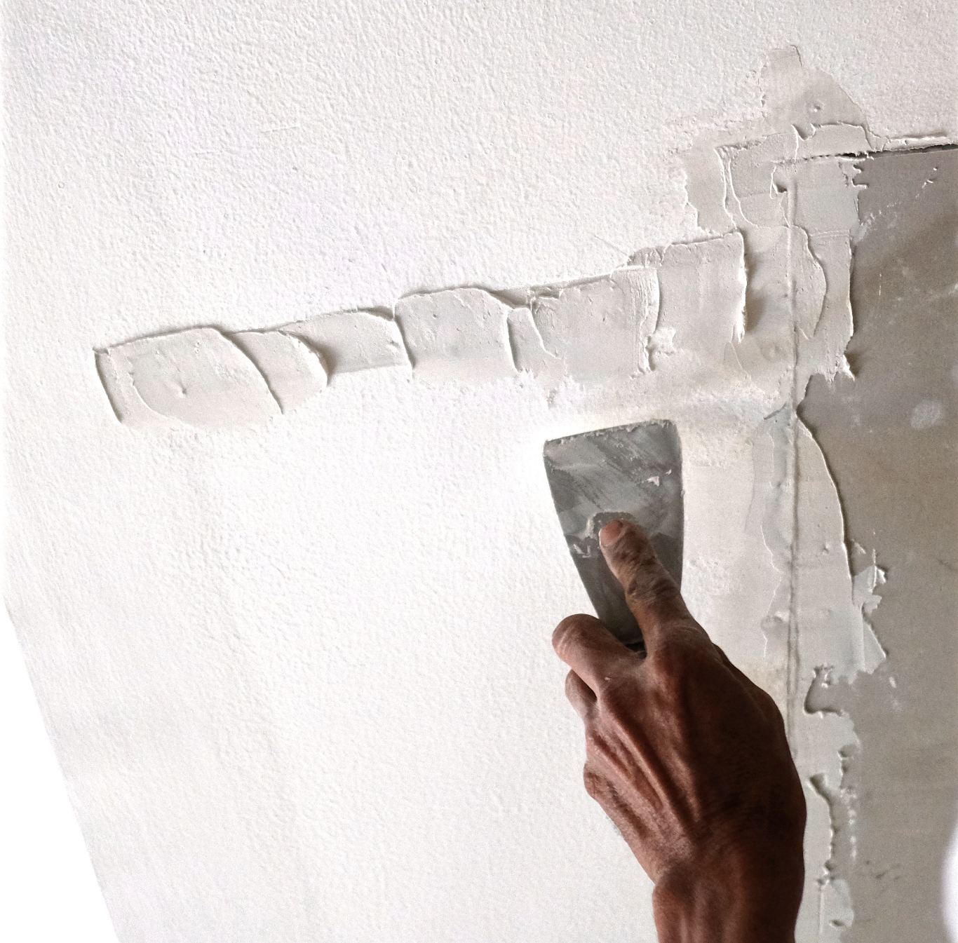 A person using a putty knife to apply plaster on a white wall.