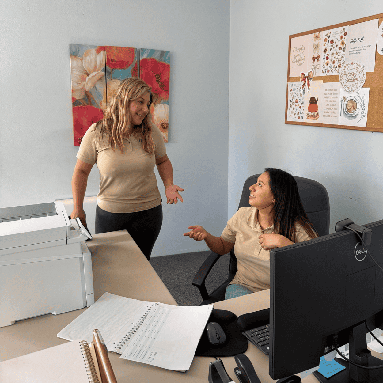 Two women in an office; one stands and gestures, while the other sits and talks.