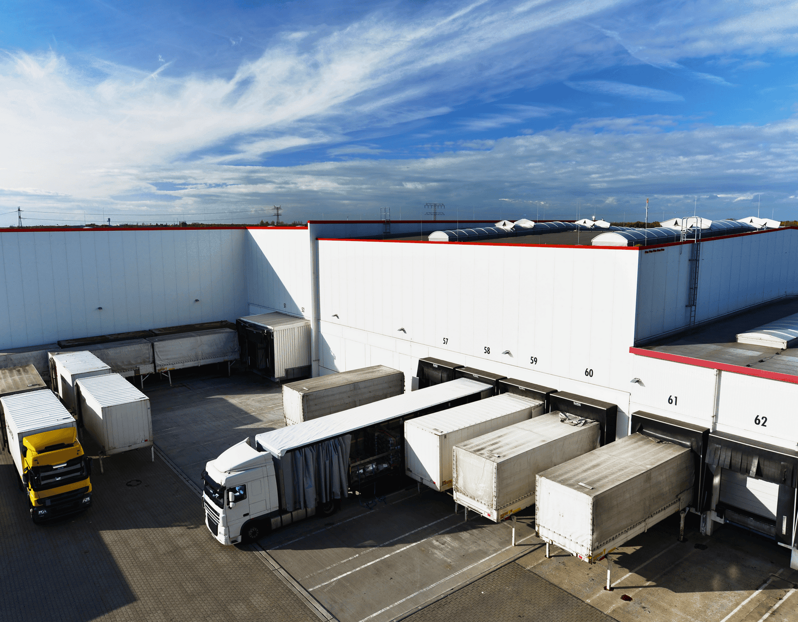 Trucks loading and unloading at a large white warehouse with a blue sky overhead.