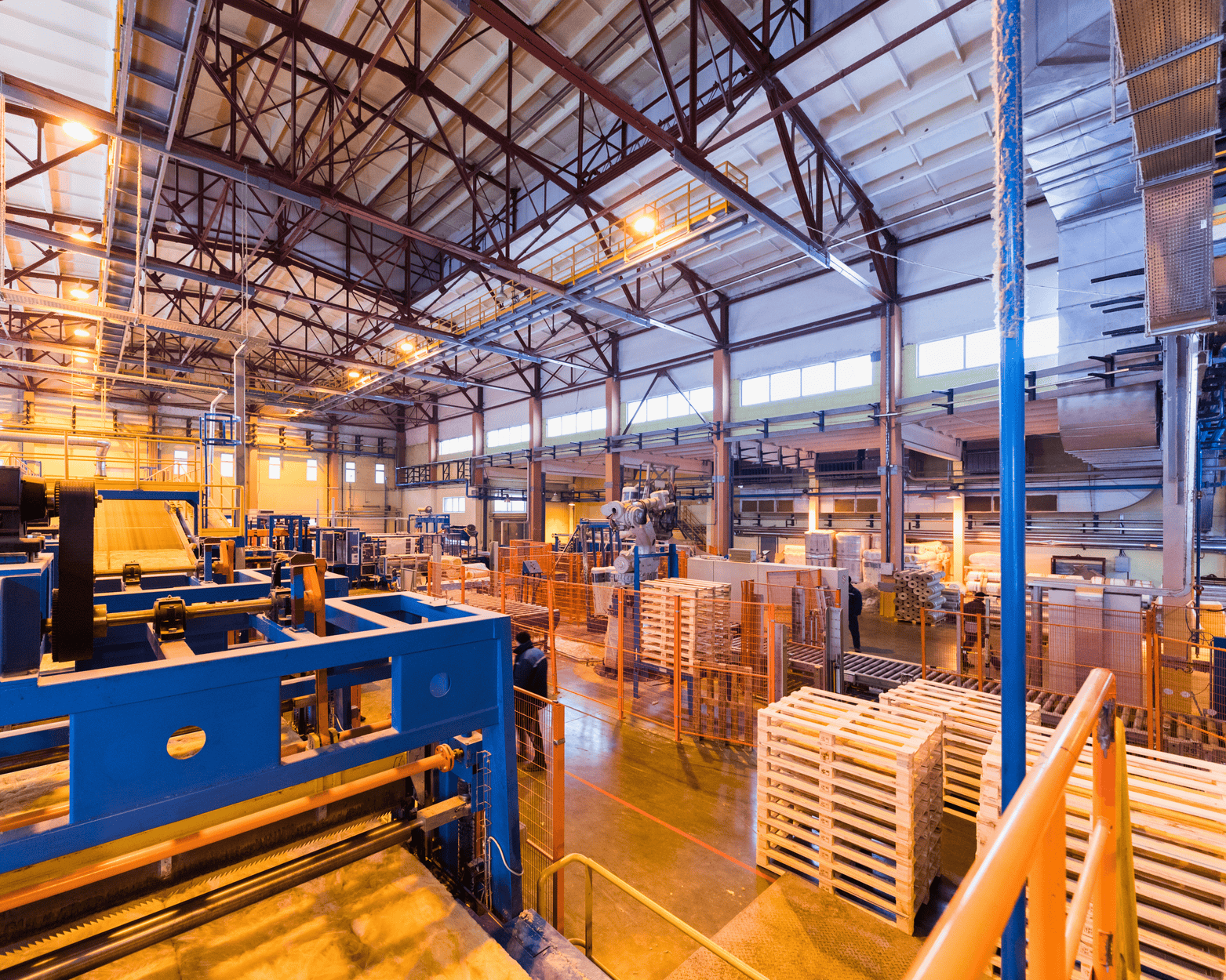 Large industrial warehouse interior with machinery, wooden pallets, and structural beams.