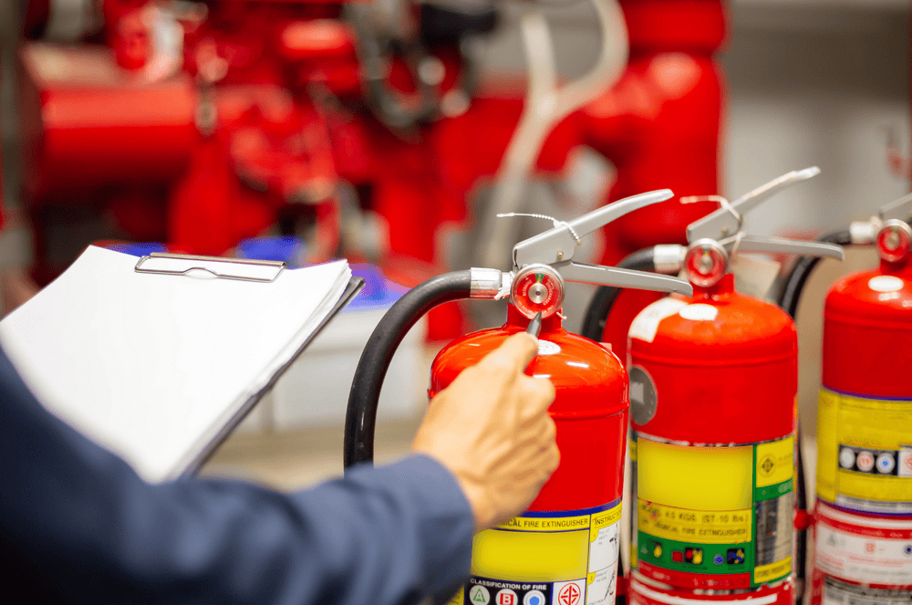 Person checking fire extinguishers in a red-colored room; clipboard in hand.