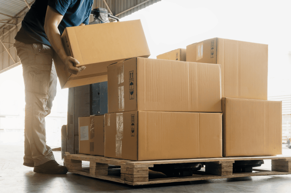 Person stacking cardboard boxes on a pallet in a warehouse.
