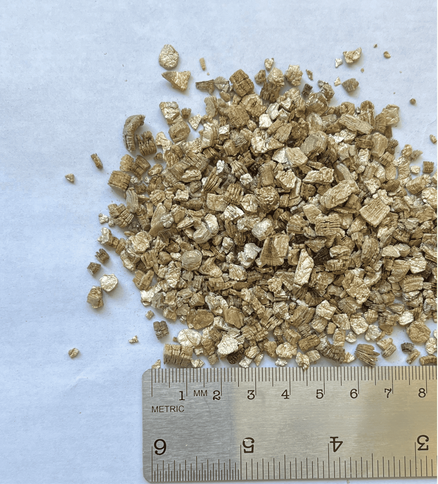 Pile of gold-colored vermiculite granules with a ruler for scale.