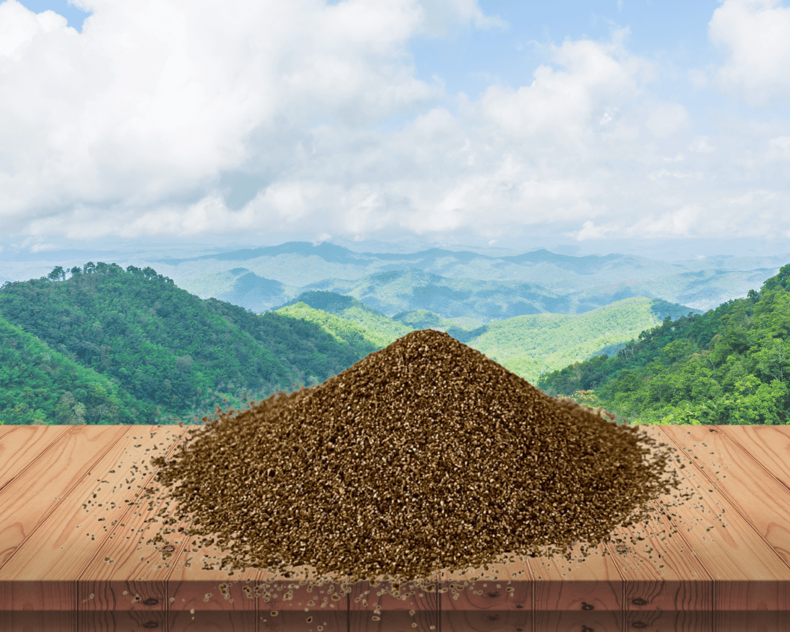 Pile of brown, granular material on a wooden surface, mountains in the background with a cloudy sky.