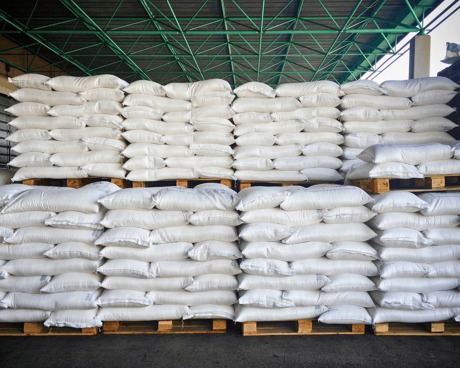 Stacks of white bags on wooden pallets inside a warehouse.