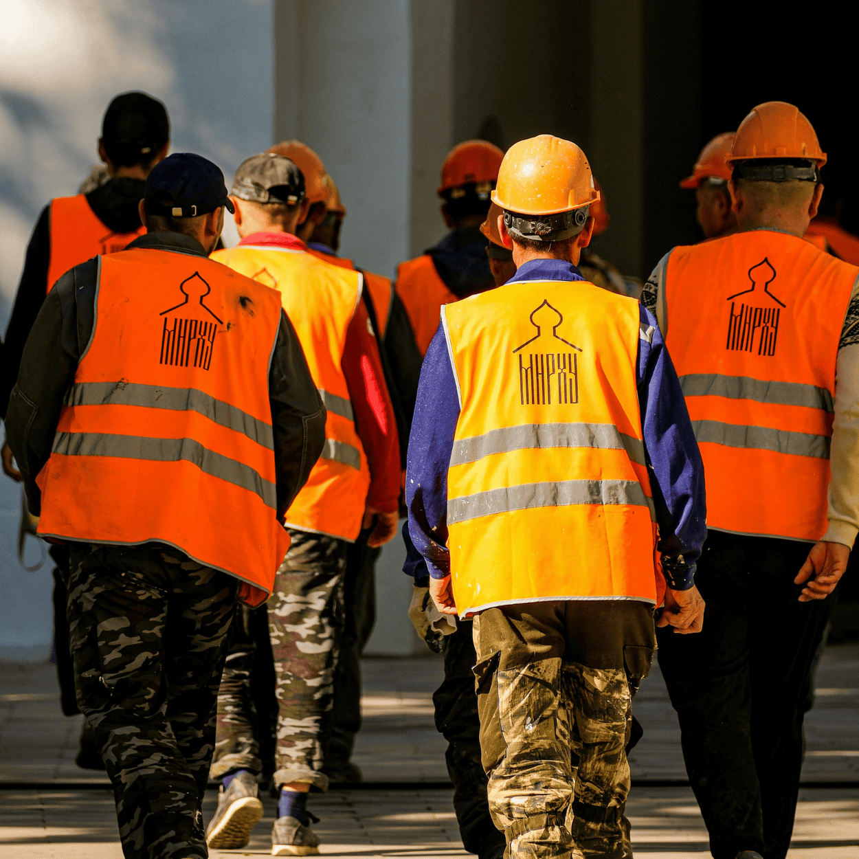 Workers in orange vests and hard hats walking toward a building.