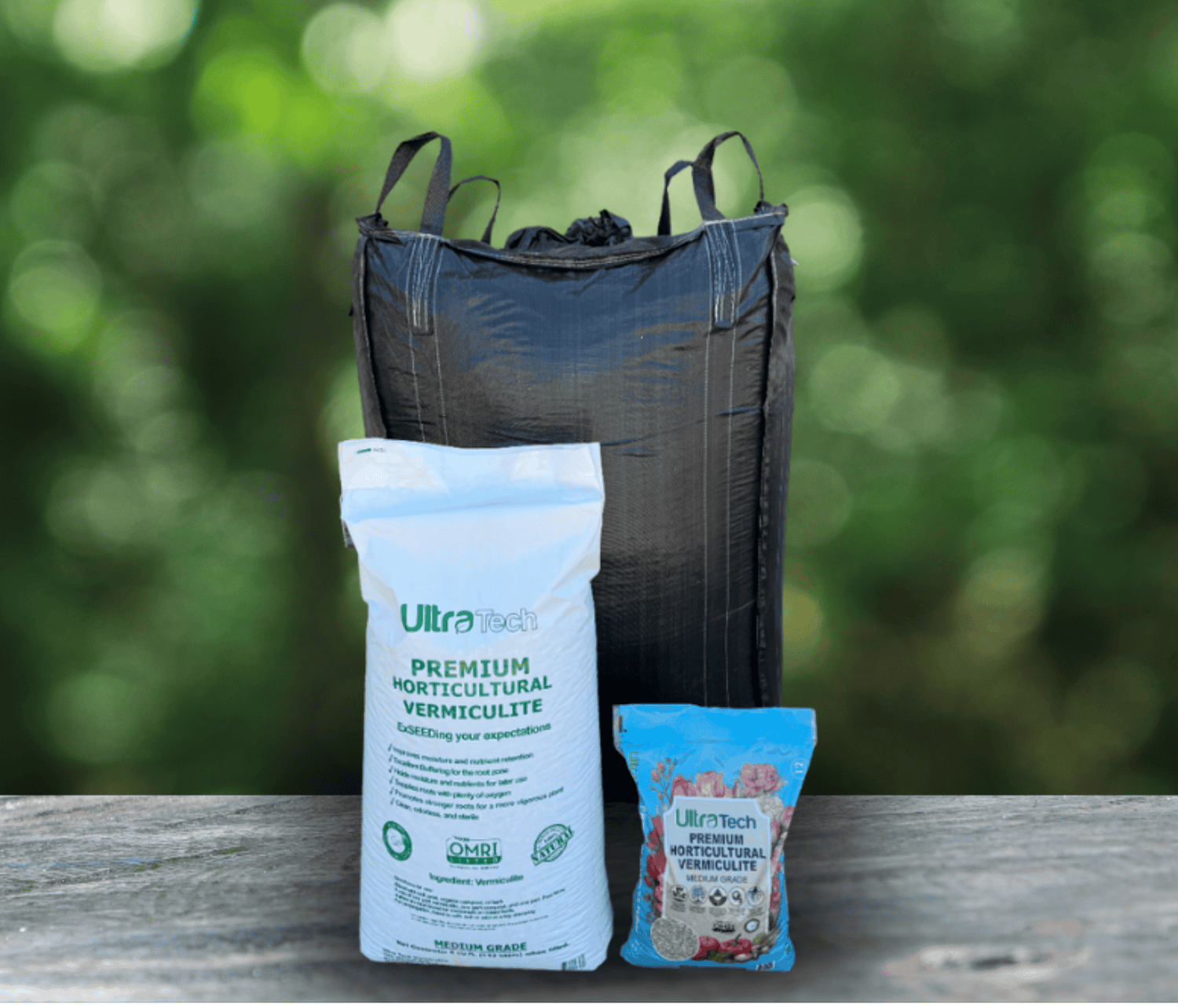 Black bulk bag and two white and blue bags of horticultural vermiculite on a wooden surface, blurred green background.