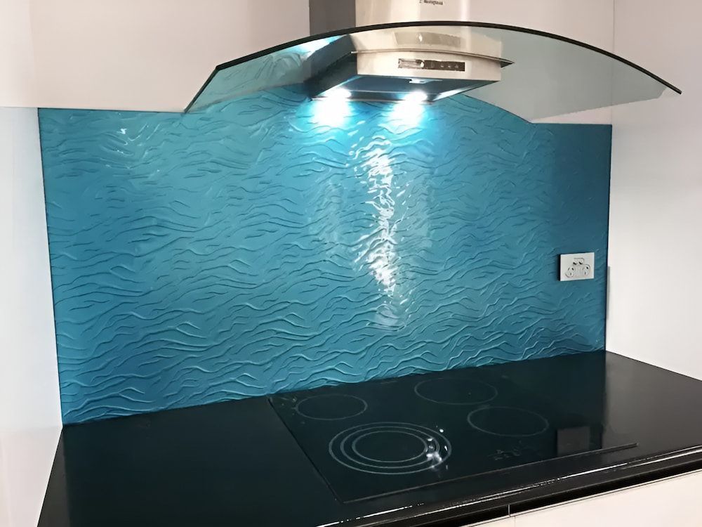 A Black Stove Top With A Blue Backsplash And A Hood Above It — Hayes & Swinburn Glass in Westcourt, QLD