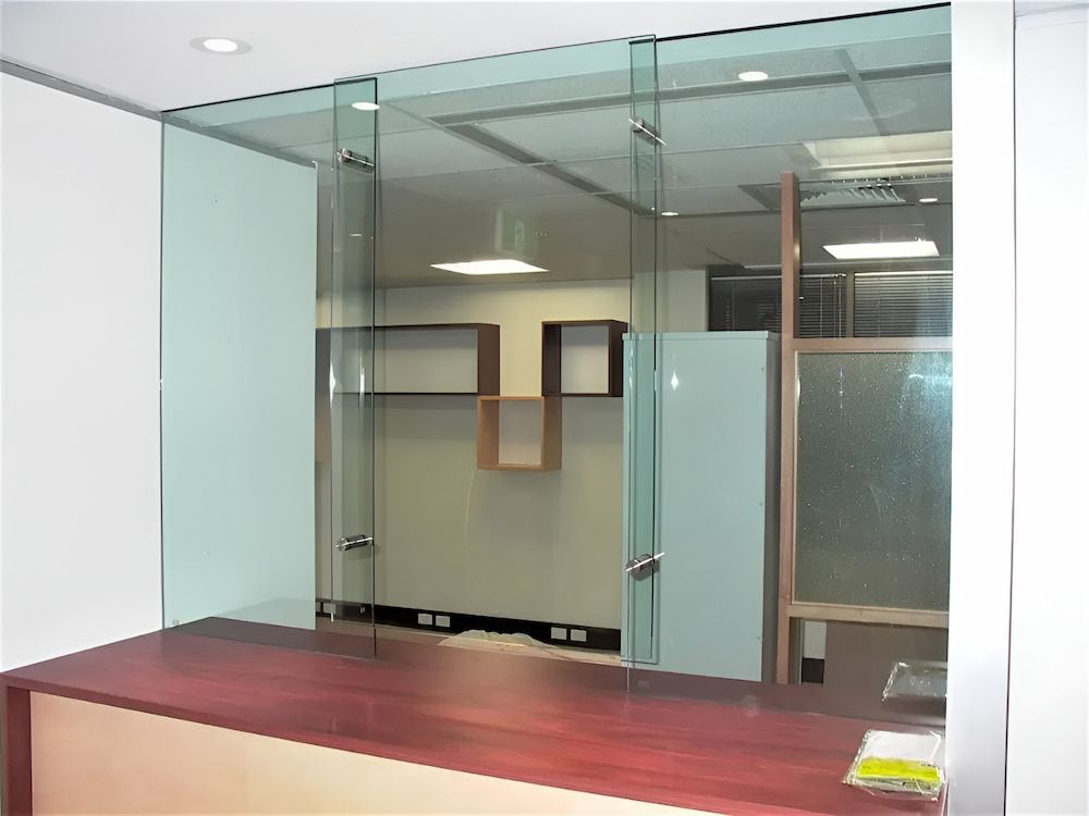 A Glass Wall With A Wooden Counter In Front Of It — Hayes & Swinburn Glass in Westcourt, QLD