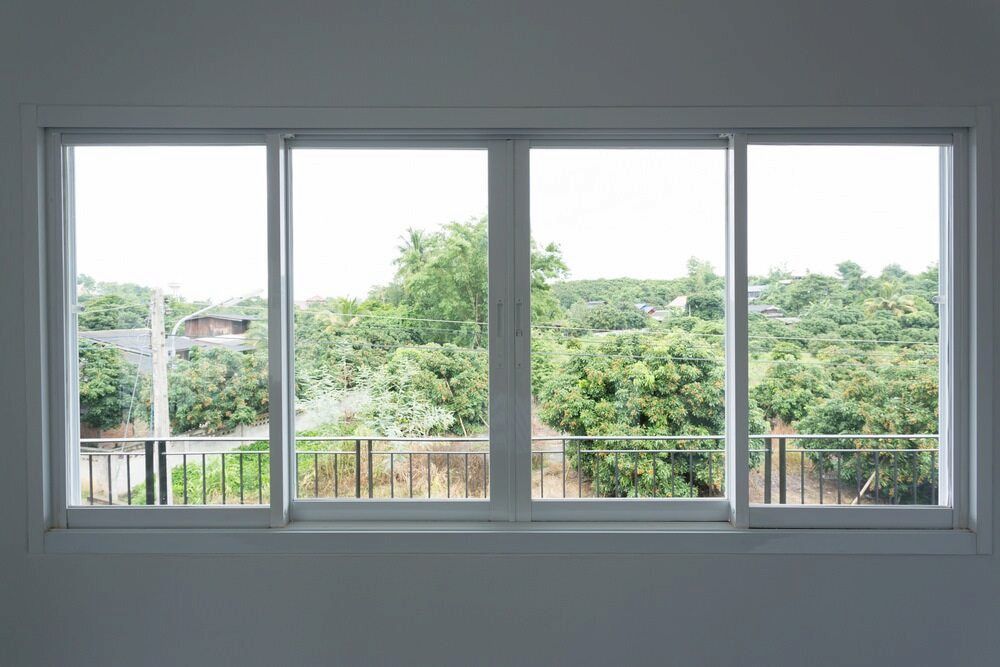A Large White Window With A View Of Trees And A Balcony — Hayes & Swinburn Glass in Westcourt, QLD