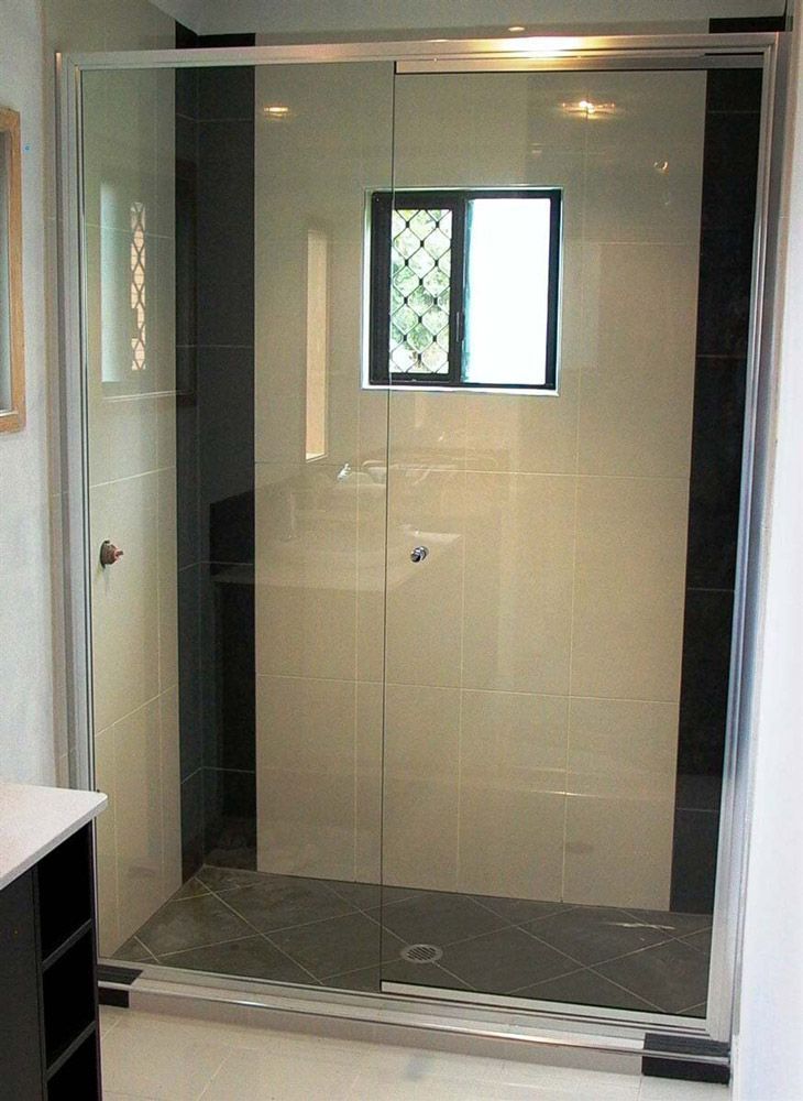 A bathroom with a sliding glass shower door and a window — Hayes & Swinburn Glass in Westcourt, QLD