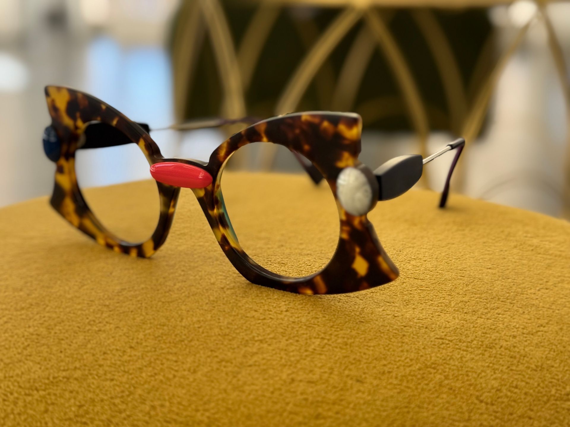 Occhiali con montatura in tartaruga e decorazioni colorate poggiano su una superficie gialla.