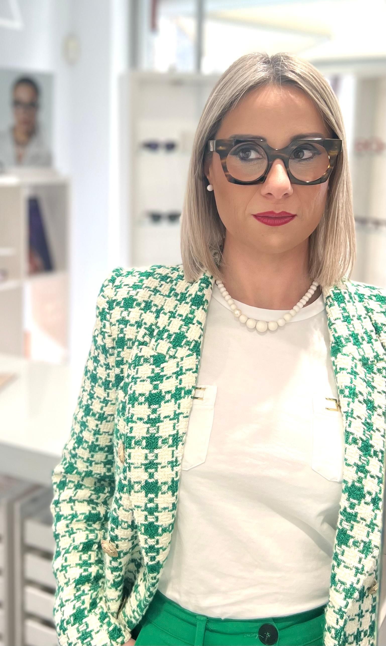 Donna con occhiali e giacca verde e bianca nello studio di un ottico.