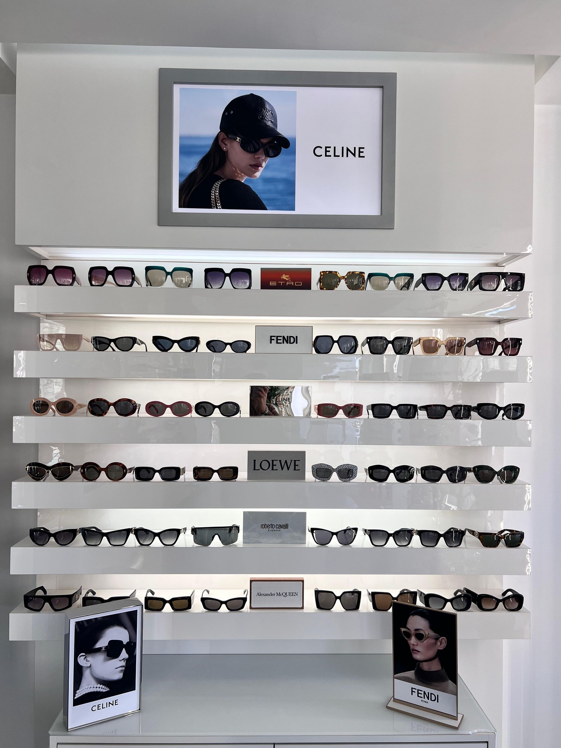 Gli occhiali da sole sono esposti su scaffali bianchi con una pubblicità di Celine in alto.