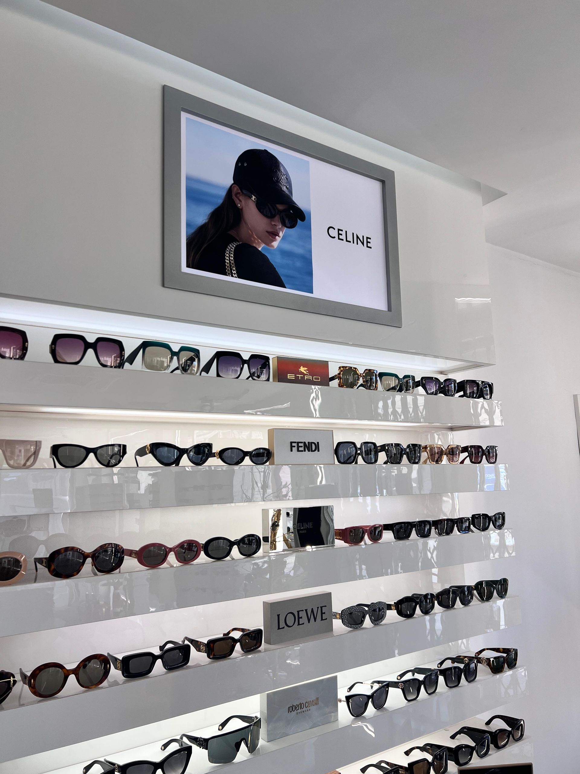 Occhiali da sole esposti sugli scaffali di un negozio al dettaglio, con una pubblicità di Celine sopra.