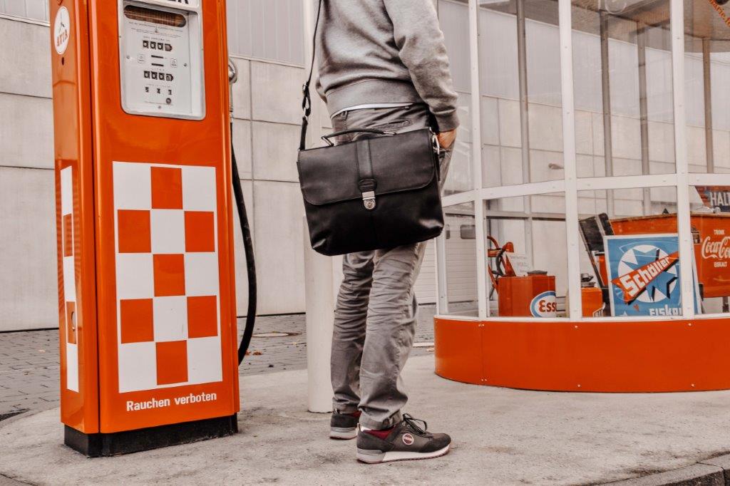 Ein Mann steht mit einer Aktentasche in der Hand vor einer Zapfsäule.