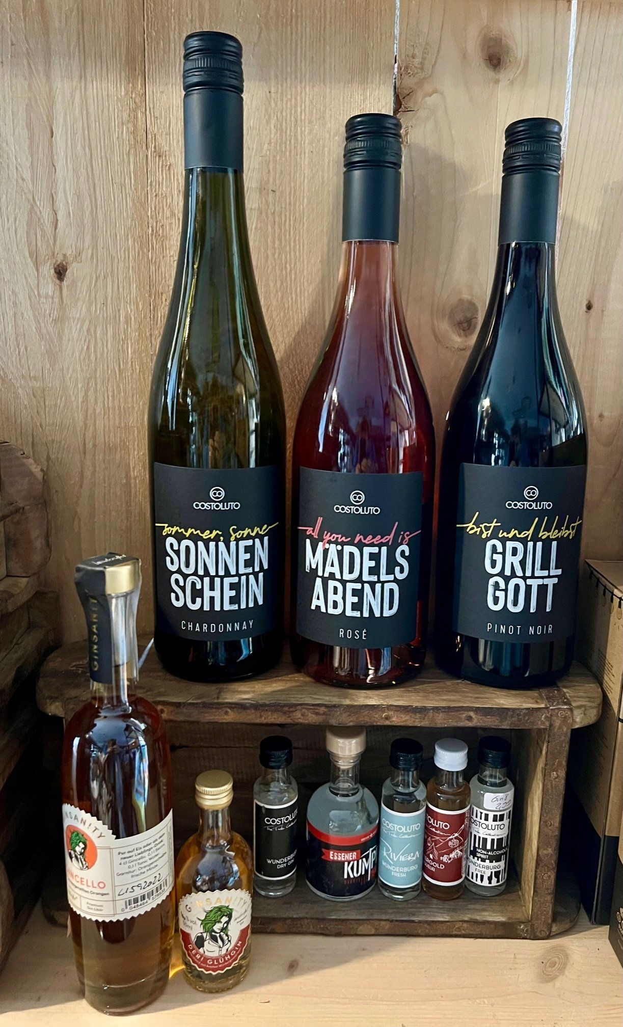 Drei Flaschen Wein stehen auf einem Holzregal.