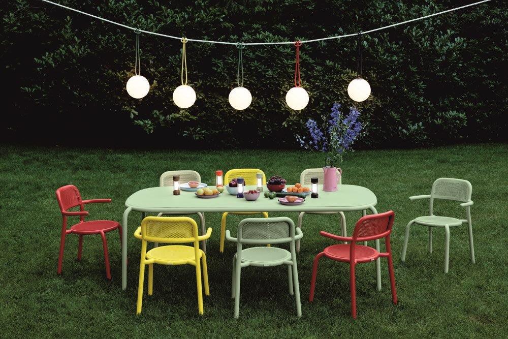 Ein Tisch und Stühle stehen im Gras unter einer Lichterkette.