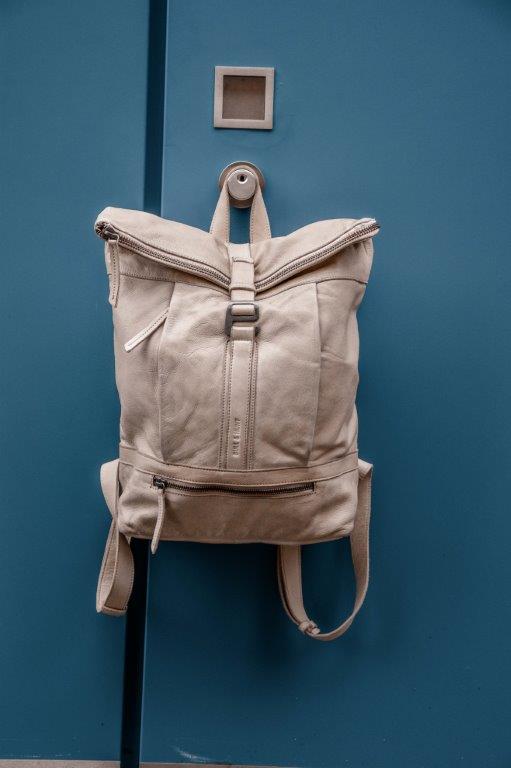 An einer blauen Tür hängt ein weißer Rucksack.