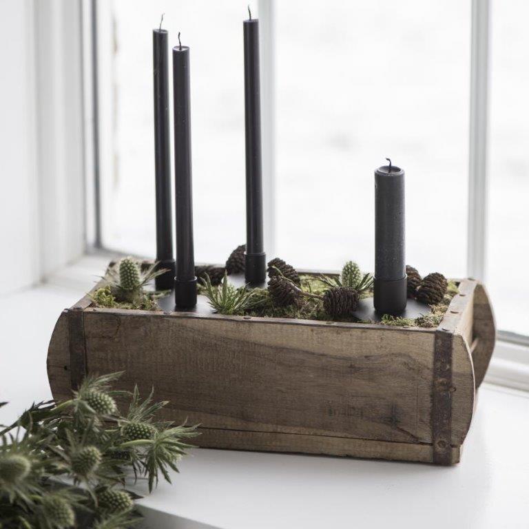 Auf einem Fensterbrett steht eine Holzkiste voller Kerzen und Pflanzen.
