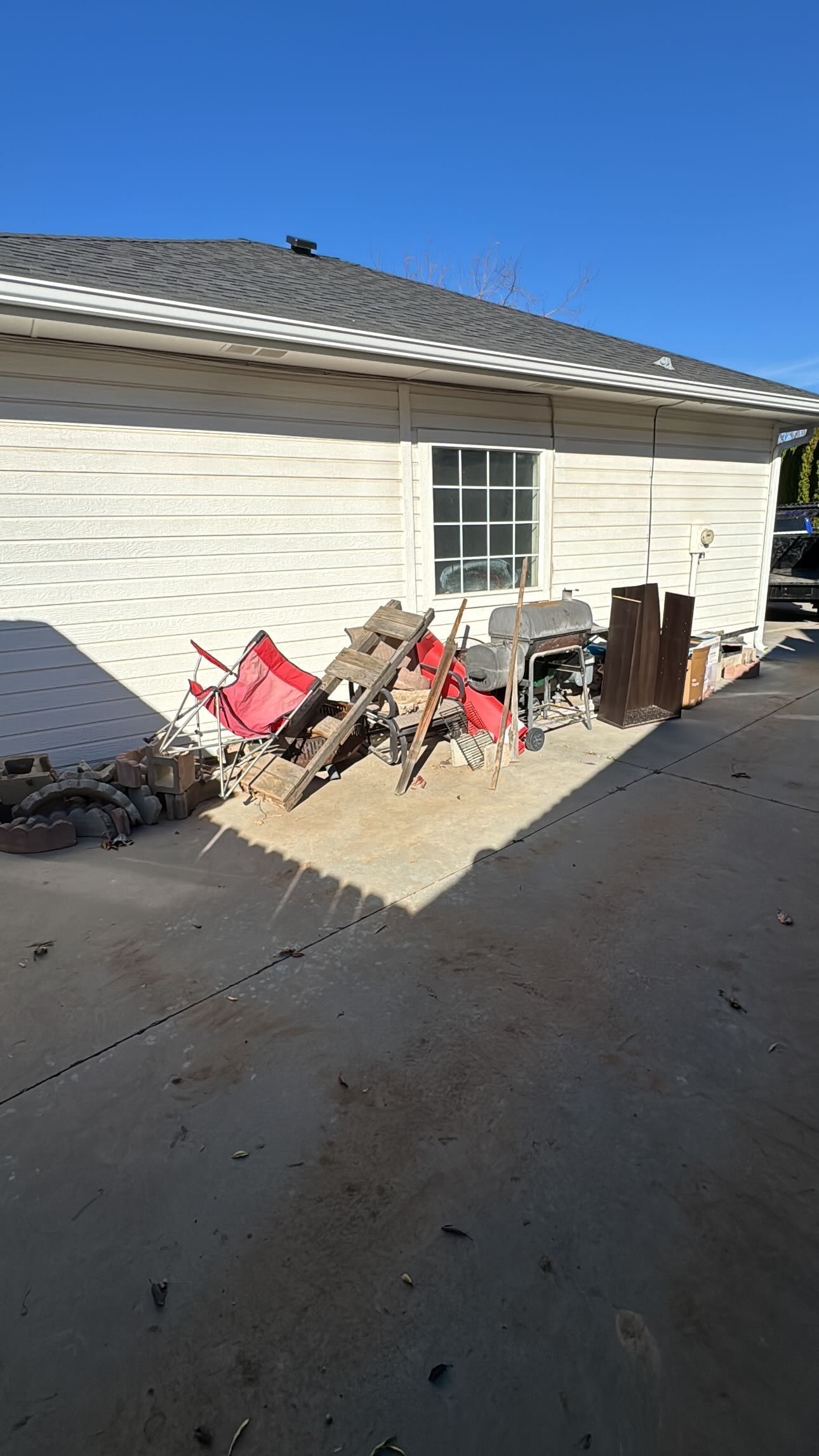 Pile of debris, including wood and red chairs, in a side yard next to a light-colored building.