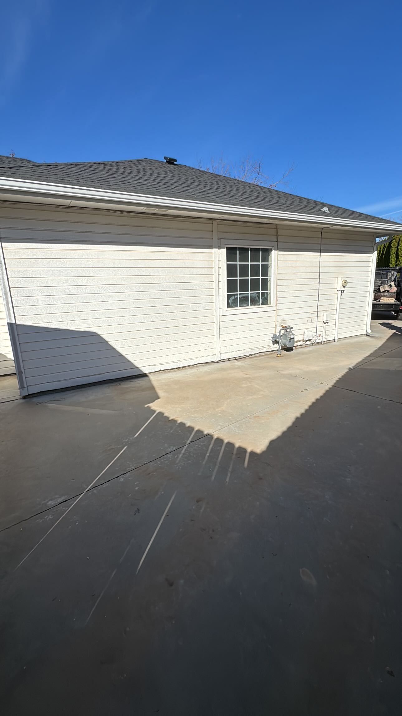 White building with a window, dark roof, and concrete ground under a bright blue sky.