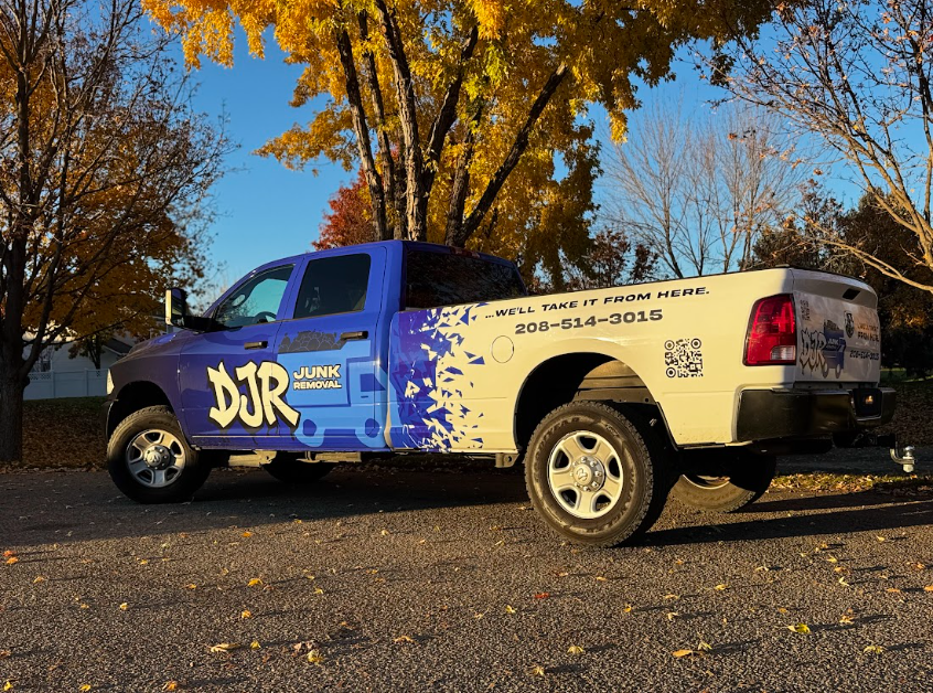 Blue and white DJR truck parked on a road with fall foliage in the background.