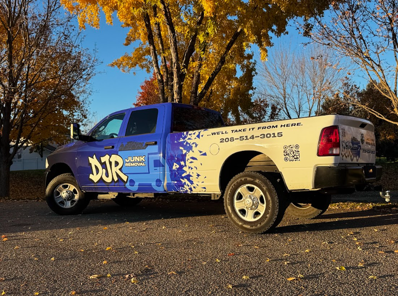Blue and white DJR truck parked on a road with fall foliage in the background.