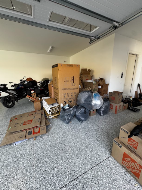 Garage interior filled with boxes, trash bags, and a motorcycle.