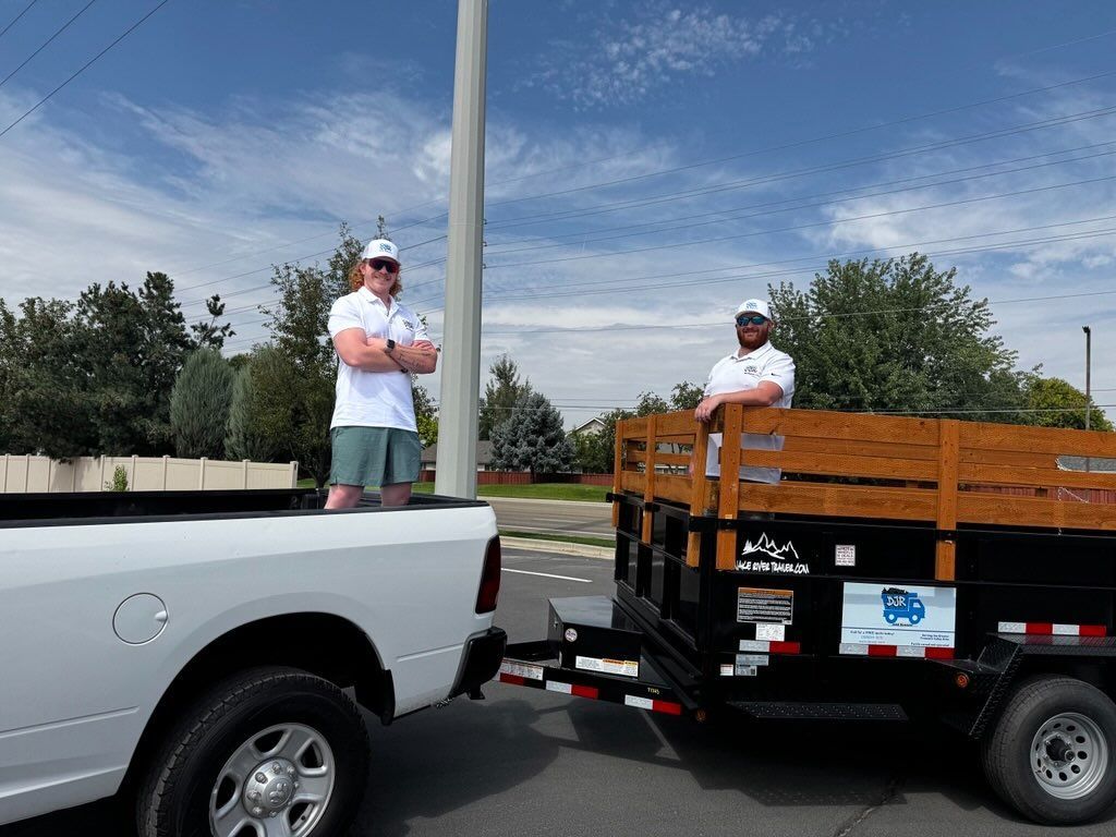 Two men in white shirts and hats with a trailer attached to a pickup truck, standing outside.