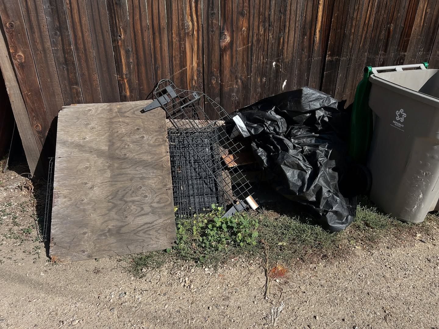 Stone slab and trash beside a wooden fence and a recycling bin.