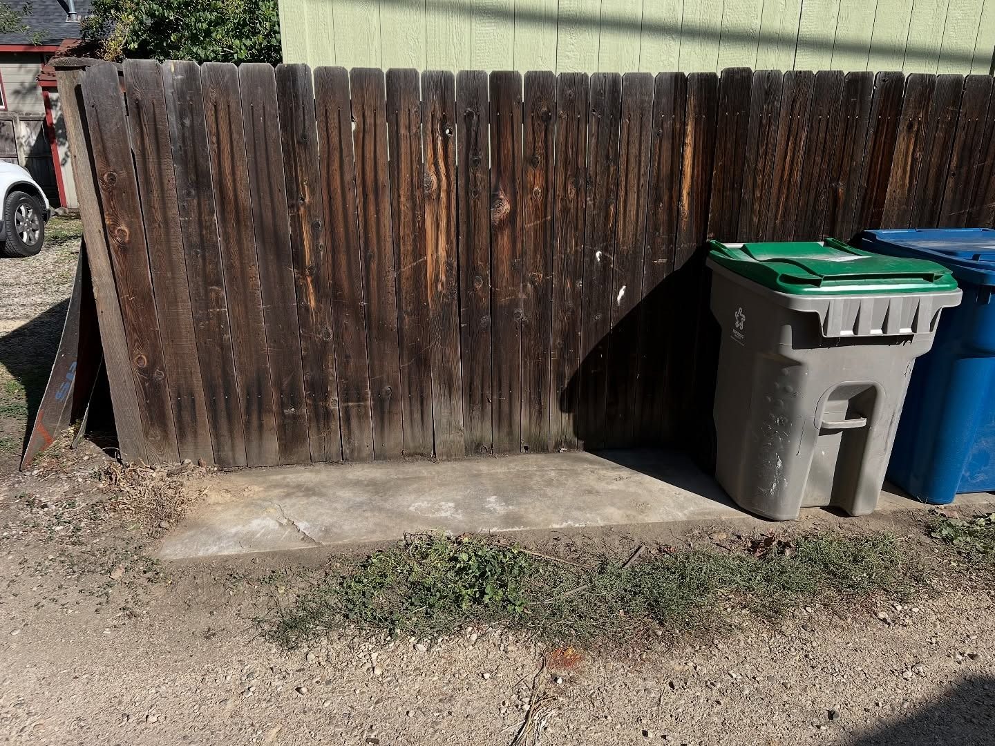 Wooden fence with two trash bins next to it on a concrete pad.