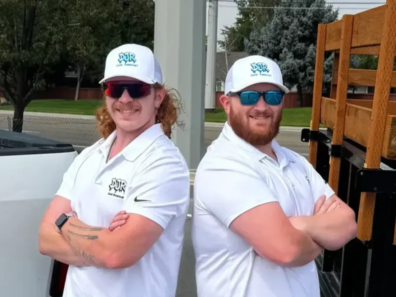 Two men in white shirts, hats, and sunglasses standing outdoors with arms crossed.