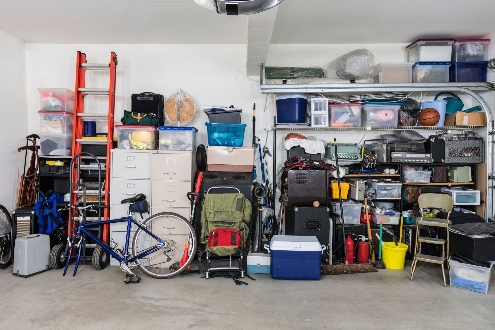 Cluttered garage interior filled with storage bins, tools, and a bicycle.