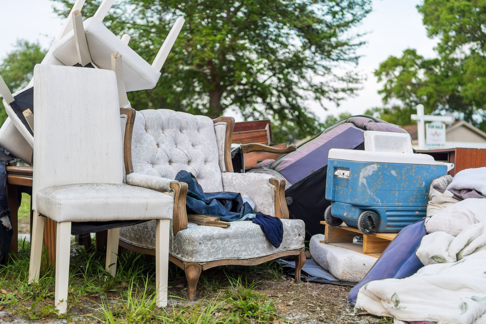 Pile of discarded furniture outside: chairs, a couch, cooler.