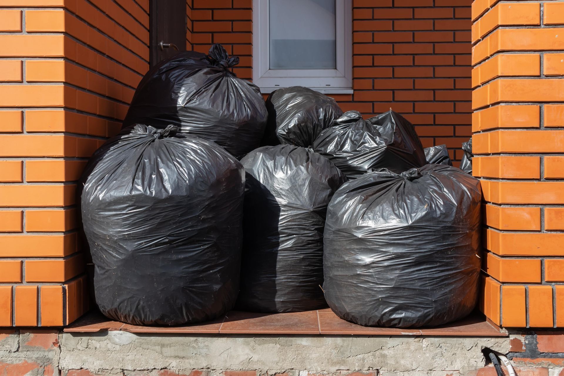 Black trash bags piled on a brick porch.