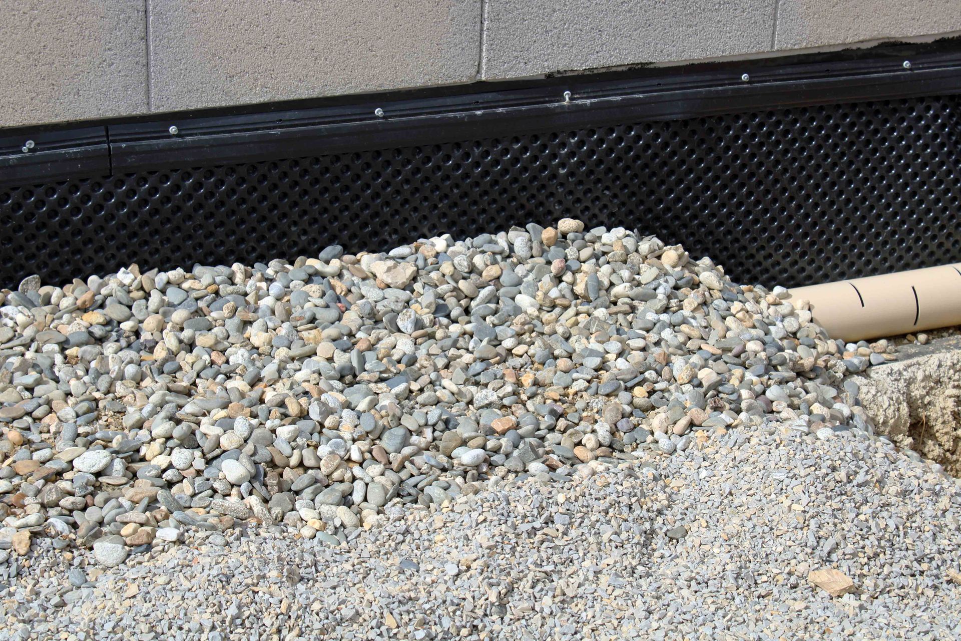 Foundation drainage system: gravel, perforated black drainage membrane, and corrugated pipe.