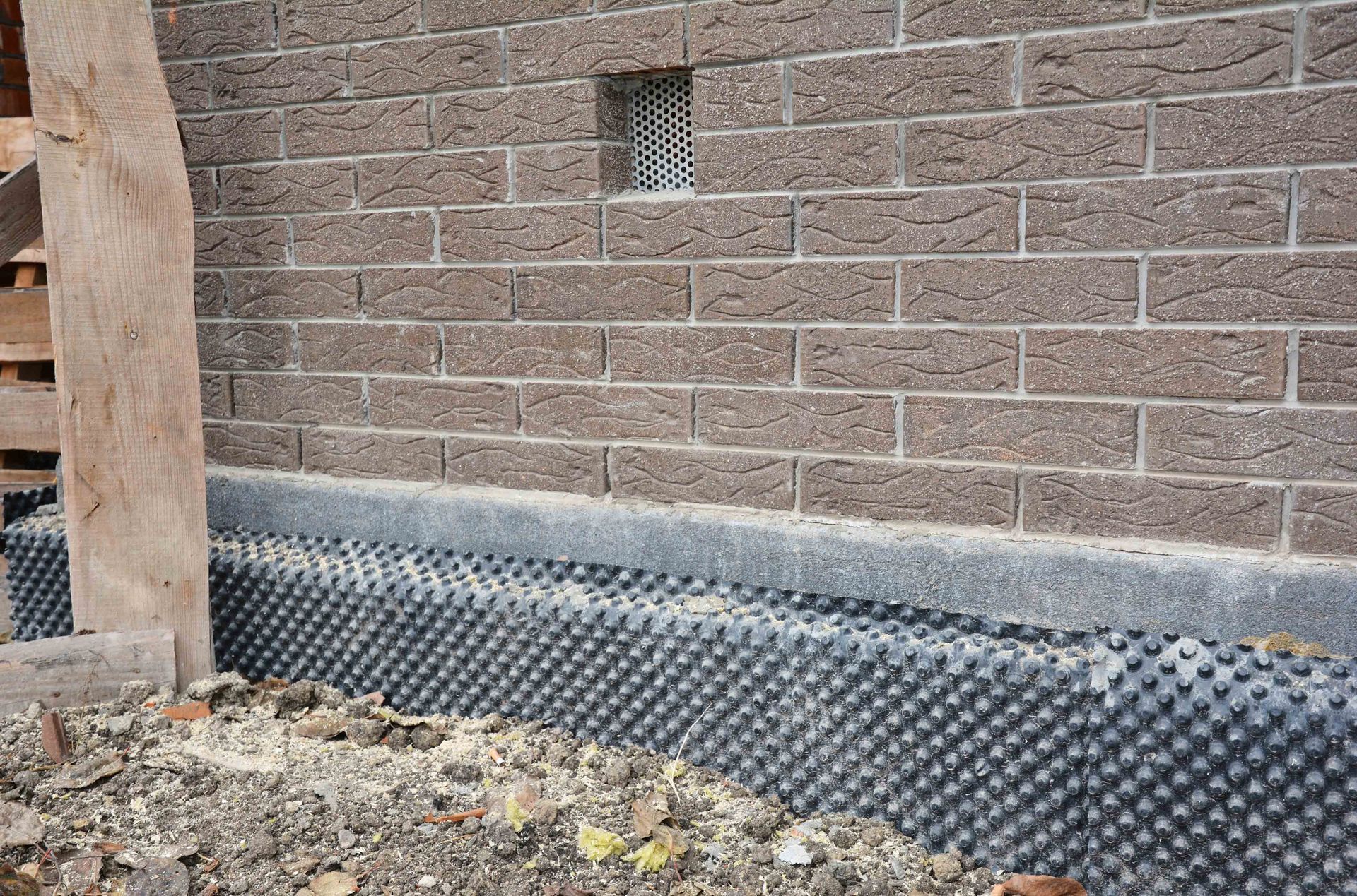 Brick wall with drainage membrane at the base, next to a wooden support post.